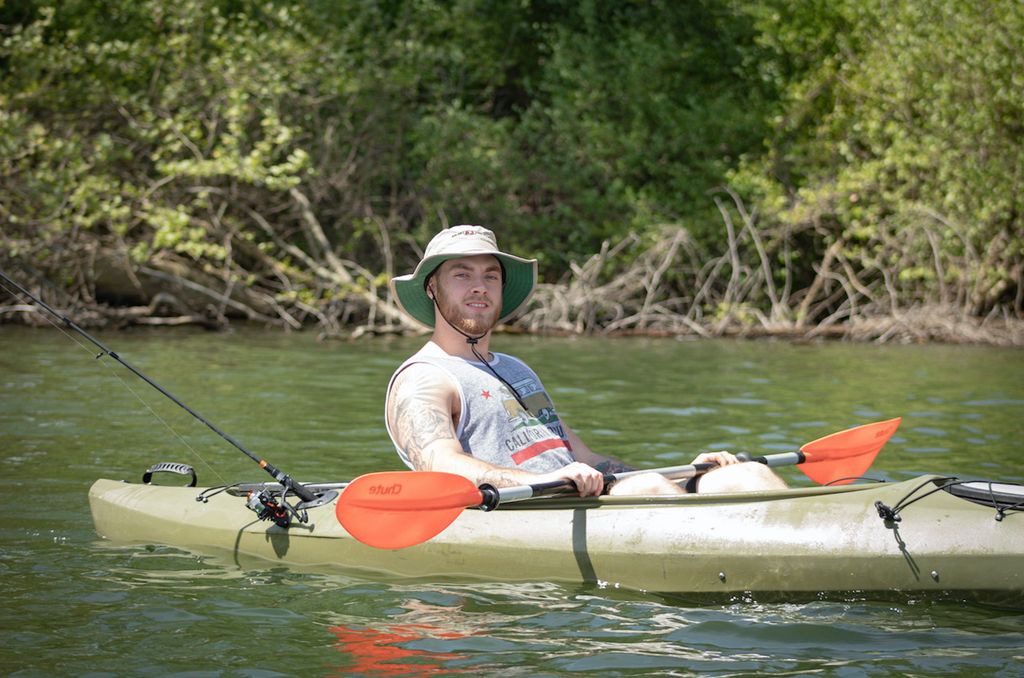 A man in a hat enjoys a peaceful day kayaking and fishing on a sunny river.